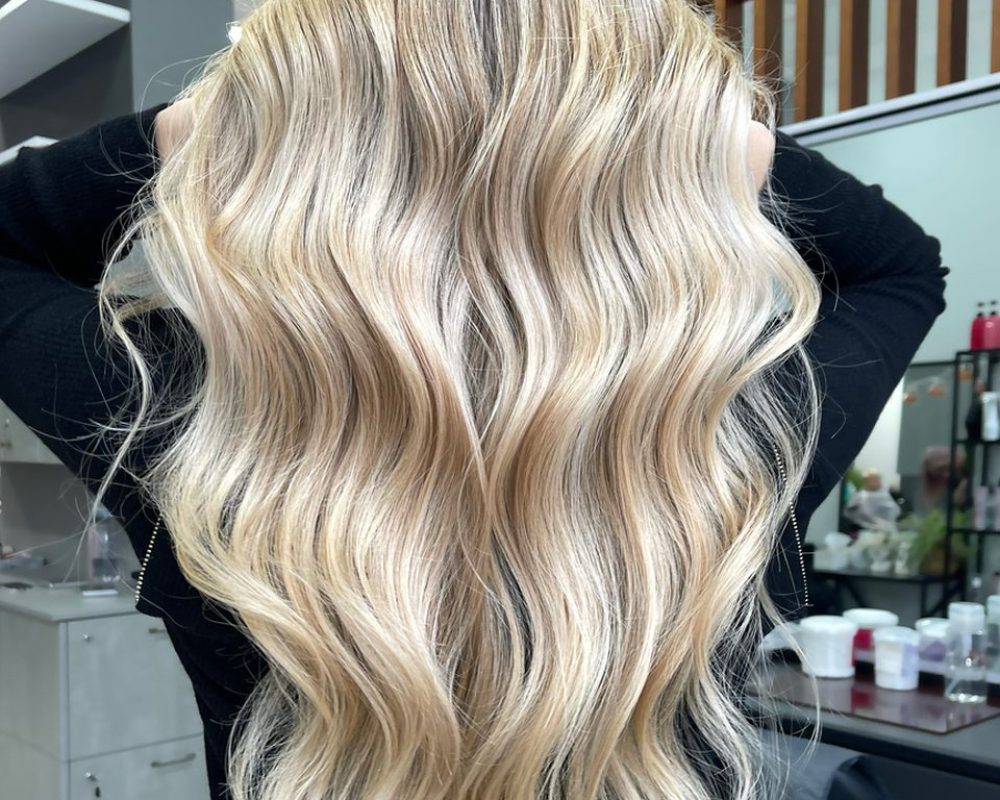 Back view of a person with long, blonde balayage hair in loose waves